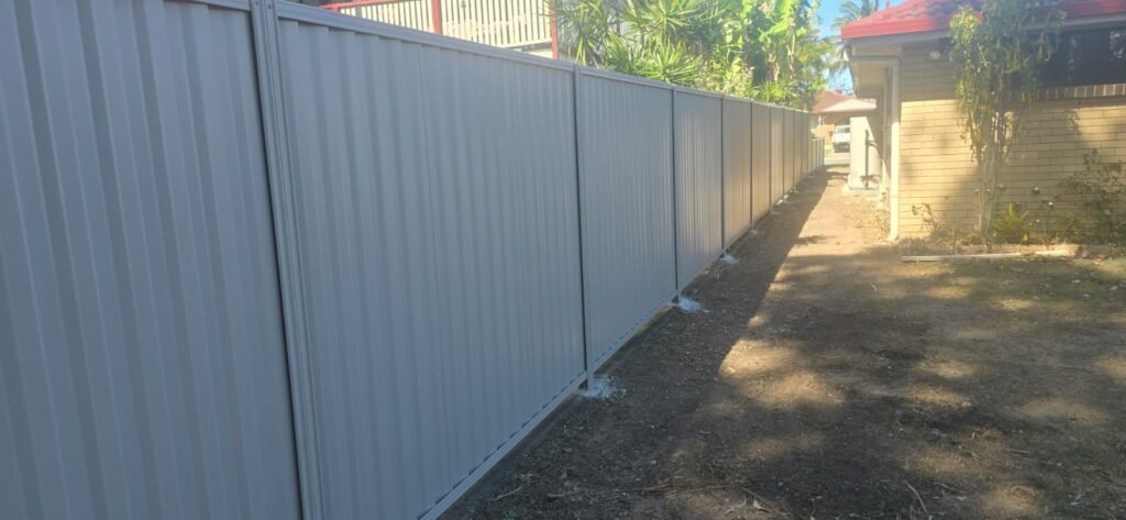Long side boundary run of GramLine® steel fencing in Birch beside a brick house, supplied by Accolade Fencing Deception Bay