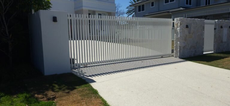 Surfmist RAD batten aluminium sliding gate closed across a driveway beside a rendered pillar, custom manufactured by Accolade Fencing