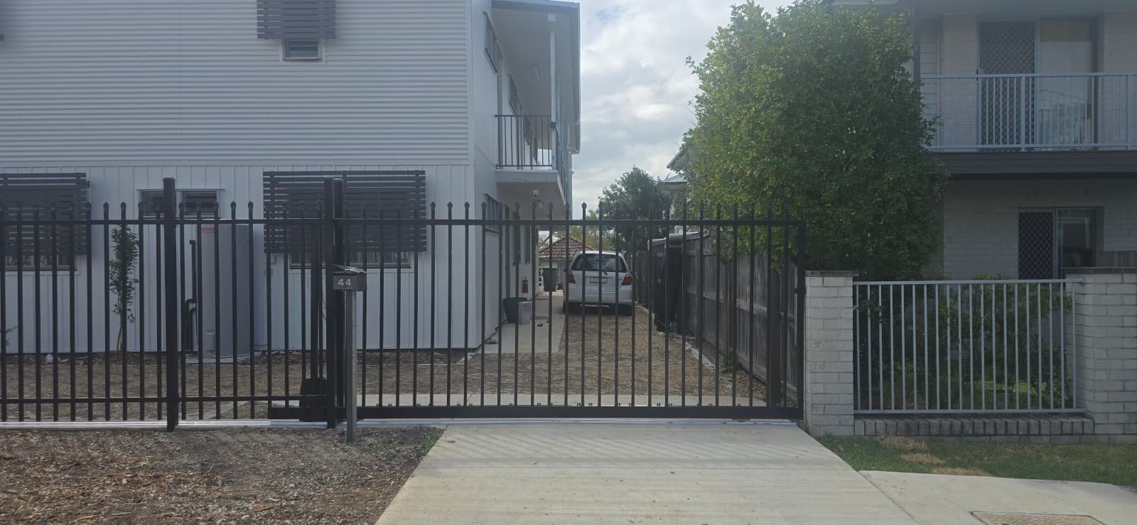 Custom Zeus aluminium sliding gate in black powder coat across a residential complex driveway, 25mm square pickets with pressed spear tops, fabricated by Accolade Fencing Deception Bay