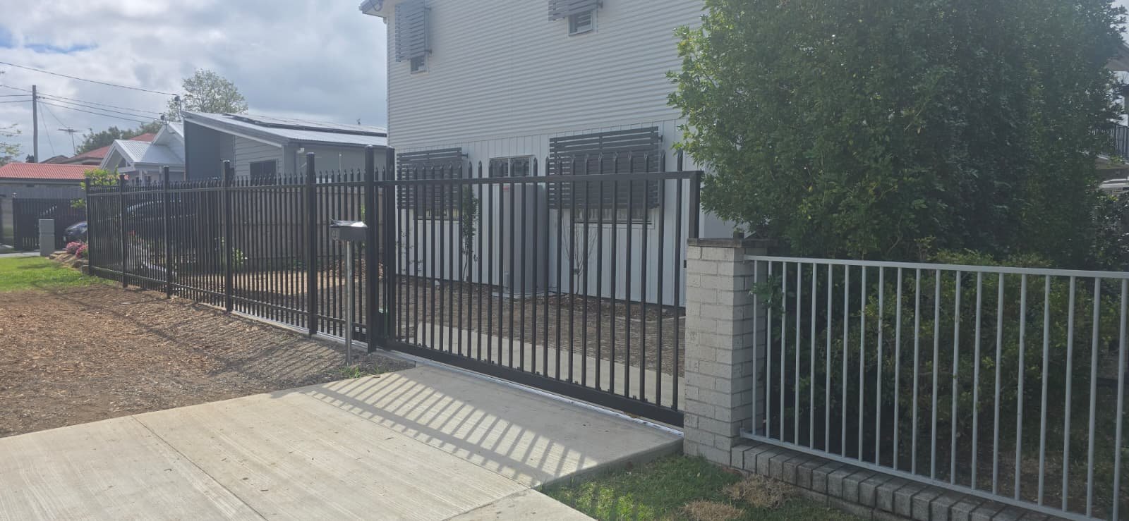 Black Zeus spear top aluminium sliding gate closed across a concrete driveway, in line with the matching spear top fence panels beyond, custom welded by Accolade Fencing